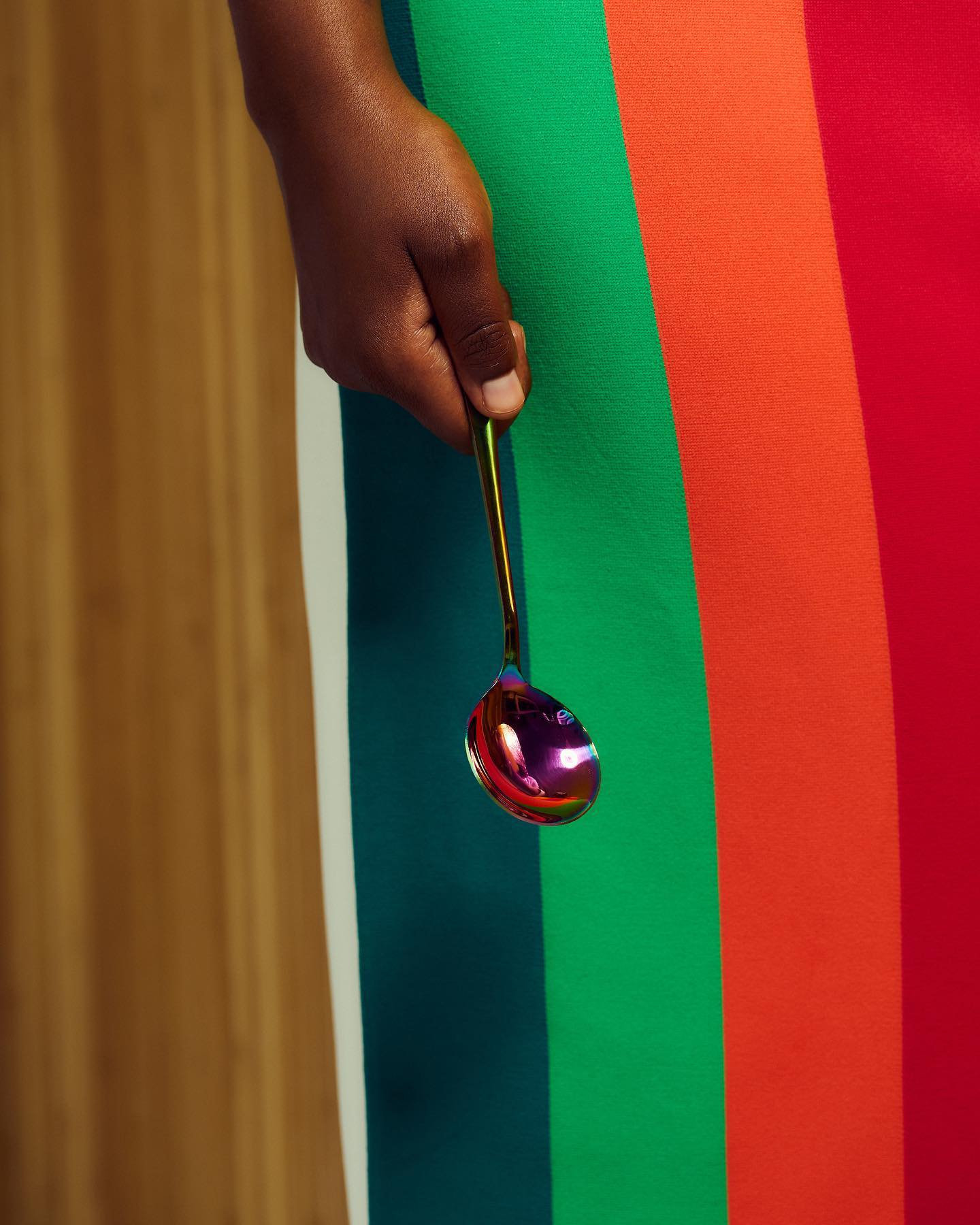 A hand holding an iridescent spoon against bold colour stripes